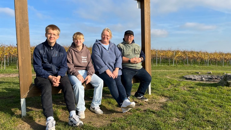 Eine Frau, ein Mann und zwei Jungs sitzen auf einem Holzrahmen auf einer Wiese.