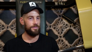 Mann mit Kappe, Bart und schwarzem T-Shirt wird interviewt