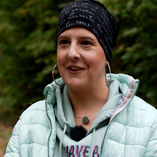 Junge Frau mit Stirnband in schwarz und heller, blauer Jacke in einem Wald stehend
