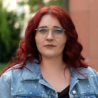 Junge Frau mit roten Haaren und Brille vor rotem Gebäude