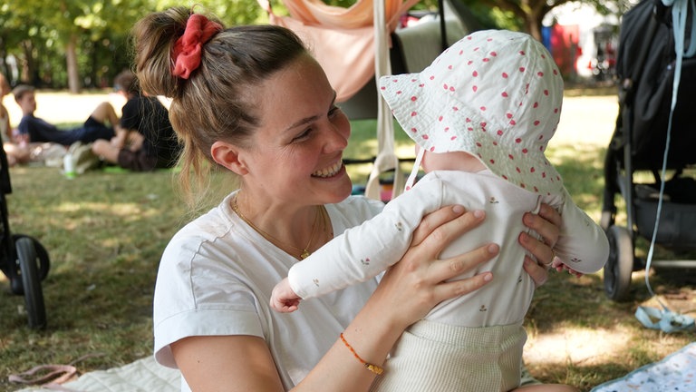 Foto von der Picknickdecke, wo man im Hintergrund Leonie sitzen sieht. Vor ihr liegt eine Spielzeug-Ananas.