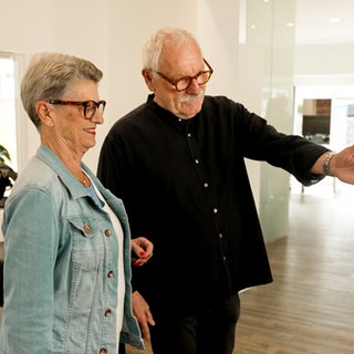 Ein Friseur weist eine Kundin im Salon auf ihren Platz. Ein Kurzhaarschnitt für eine Frau macht Friseur Karlheinz in den 1970ern bekannt.