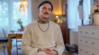 Junger Mann mit Mütze in einem Wohnzimmer auf einem Stuhl sitzend