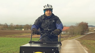 Mann fährt mit Lastenbike übers Feld