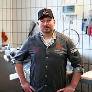 Metzgermeister und Maultaschenkänig Olli Häcker stecht in seiner Metzgerei. Er hat die Hände auf den Hüften und schaut in die Kamera.