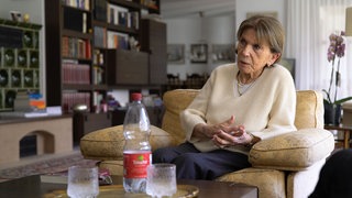Ruth ist 95 Jahre alt und Zeitzeugin des Zweiten Weltkriegs. SWR Heimat hat sie zu Hause besucht und sie erzählt von ihren Erlebnissen während dem Krieg. Sie sitzt auf dem Sofa in ihrem Wohnzimmer.