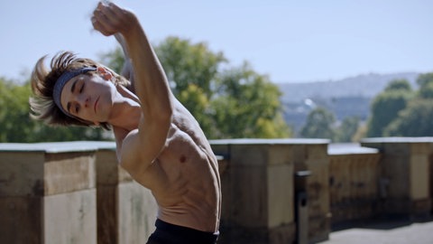 Junger Mann mit durchtrainiertem, nacktem Oberkörper in einer Tanzpose