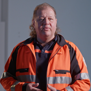 Rettungssanitäter in orangener Kleidung schaut in Kamera