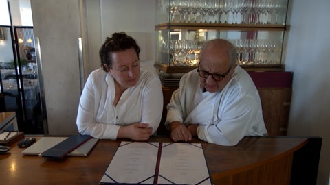 och Vincent Klink und seine Tochter Eva sitzen zusammen am Tisch und schauen auf die Speisekarte ihres Restaurants.