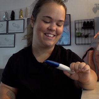 Nadine hält einen positiven Schwangerschaftstest in der Hand. Sie freut sich, dass sie jetzt zum zweiten Mal schwanger ist. 
