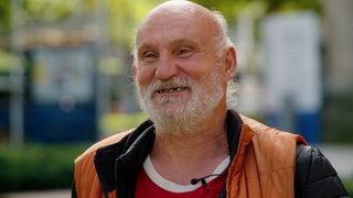 Harry Pfau steht vor „Harrys Bude” in Stuttgart und lächelt in die Kamera.