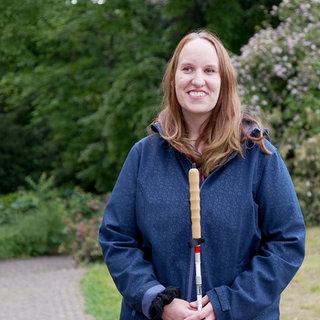  Nathalie hat einen Blindenstock in der Hand und lächelt in die Kamera. Die 25-Jährige erzählt, dass sie während dem Studium ihren Sehnerv verloren hat.
