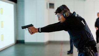 Polizei-Azubi Adam trägt eine Polizei-Uniform und trainiert das Schießen mit einer Dienstwaffe am Schießstand.