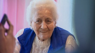 Die 90-jährige Sofia in der Wohnküche in der Pflege-WG in Stuttgart. Sie lauscht der Unterhaltung ihrer Mitbewohner und lächelt. 