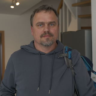 Klaus, getrennter Vater. Klaus trägt einen blauen Hoodie, über seiner linken Schulter hängt locker ein Kinderrucksack. Er schaut mit traurigen Augen in die Kamera. 