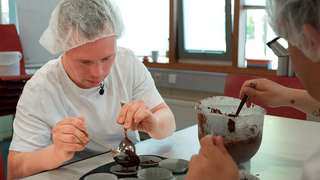 Daniel sitzt vor einer Muffinform und backt in seiner Arbeit.