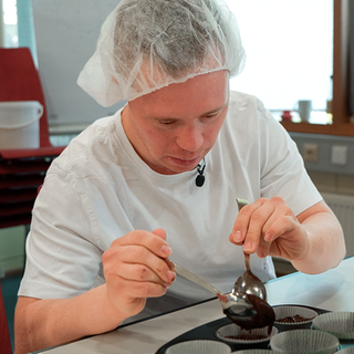 Daniel sitzt vor einer Muffinform und backt in seiner Arbeit.