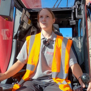 Kranführerin Annika sitzt auf einer Baustelle in ihrem Kran. 