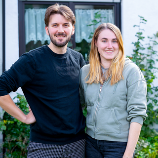 Pascal und Alina stehen vor ihrem Haus. Beide lächeln in die Kamera.