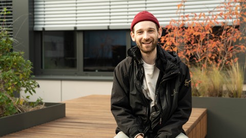 Junger Mann mit roter Mütze auf Dachterrasse sitzend