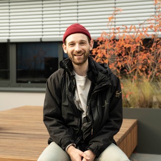 Junger Mann mit roter Mütze auf Dachterrasse sitzend