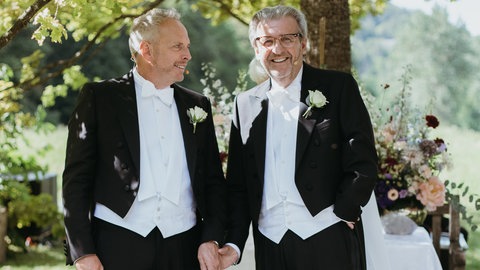 Zwei Männer im Frack halten Händchen