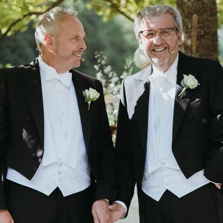 Zwei Männer im Frack halten Händchen