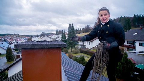Schornsteinfegerin Janina steht auf einem Dach und reinigt den Schornstein.
