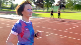 Karin ist 81 Jahre, joggt in Sportklamotten auf einem Sportplatz und gibt ein Lauftraining für Anfänger
