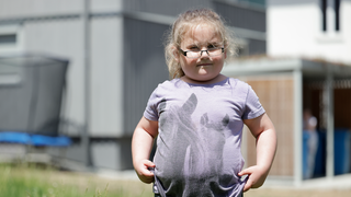 Alina ist ein sechsjähriges Mädchen mit Brille und blondem Pferdeschwanz. Sie schaut etwas scheu, aber entschlossen in die Kamera.