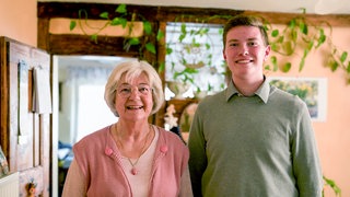 Die Freunde Margrit und Oliver stehen nebeneinander im Haus von Margrit in Leidringen und lachen in die Kamera. Sie ist 79 Jahre alt, er ist 17. 