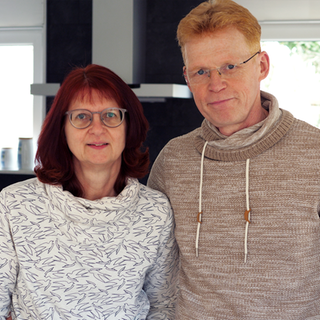 Ulrike und Gerold sind weiße Menschen in ihren 50ern. Sie trägt eine Brille und hat rötlich gefärbte Haare. Er trägt eine randlose Brille und hat hellrotes Haar.  
