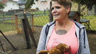 Frau mit Huhn im Arm im Freiluftgehege