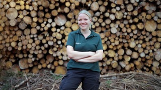 Eine junge Frau steht vor aufgestapeltem Holz.