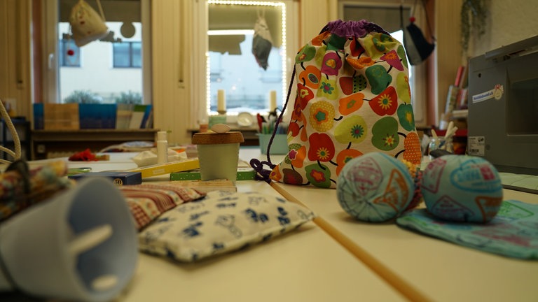 Auf einem steht ein Wohlfühlbeutel. Drum herum liegt eine Wärmflasche, zwei Bälle und andere Kleinigkeiten, die in den Beutel kommen.