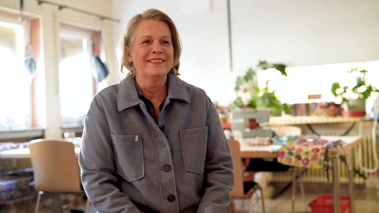 Charlotte sitzt im Vereinsraum und lächelt in die Kamera. Sie hat blonde kurze Haare und trägt ein graues Hemd.