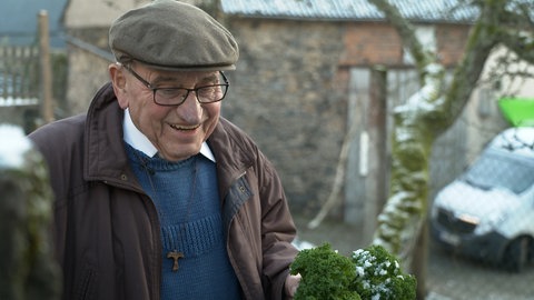 Ein alter Mann mit Mütze und Brille lacht. Albert ist seit 65 Jahren Priester im Hohen Westerwald.