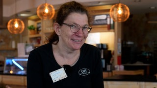 Frau mit braunen Haaren, Brille und schwarzem Shirt in Café.