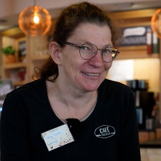 Frau mit braunen Haaren, Brille und schwarzem Shirt in Café.