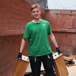 Junger blonder Mann in grünem T-Shirt mit Arbeitshandschuhen.