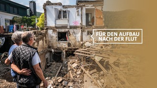 Sich umarmendes Paar schaut auf sein durch Hochwasser zerstörtes Haus in Rech an der Ahr