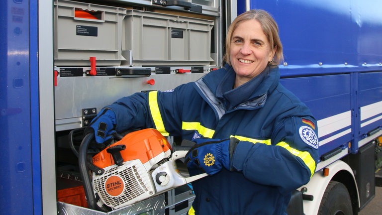 Frau in THW-Uniform hebt eine Kettensäge aus einem LKW.