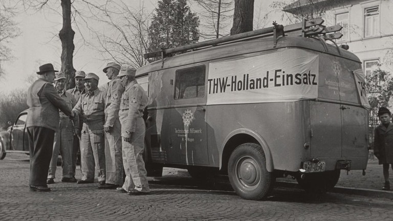 Helfer des THW stehen vor einem Fahrzeug mit der Aufschrift "THW-Holland-Einsatz".