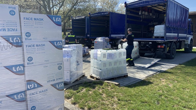 Mehrere Transporters des THW werden entladen. Davor stehen Paletten mit Schutzmaterial wie Masken.
