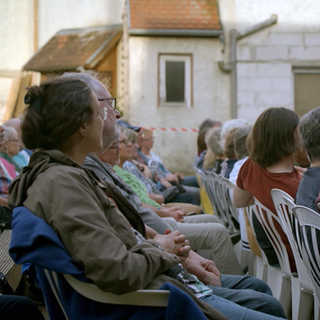 Theaterbesucher sitzen auf Plastikstühlen im Hof