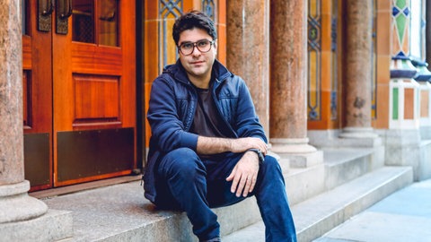 Der Theaterautor Nassim Soleimanpour auf einer Treppe sitzend.