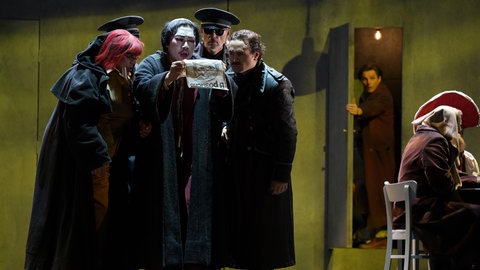 vorne v.l.n.r. Peter Marsh (Missail), Inho Jeong (Warlaam) und Morgan-Andrew King (Mikititsch) sowie Dmitry Golovnin (Grigori Otrepjew; im Hintergrund in der Tür) und Ensemble