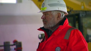 Axel Milberg bei den Dreharbeiten zu "Verschollen". Er ist auf der Baustelle von Stuttgart 21 und trägt eine orangene Warnweste und einen Helm.