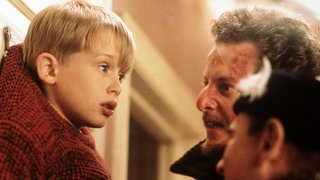 Mccauley Culkin als "Kevin allein zuhaus" hängt mit dem Pullover an einem Haken. Die beiden Einbrecher stehen vor ihm.