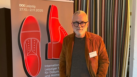 Der Leiter des Dokumetarfilm-Festivals DOK Leipzig, Christoph Terhechte, steht vor einem Plakat zur 68. Auflage des Festivals.